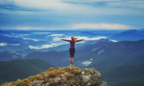 Young woman on a stone with raised hands